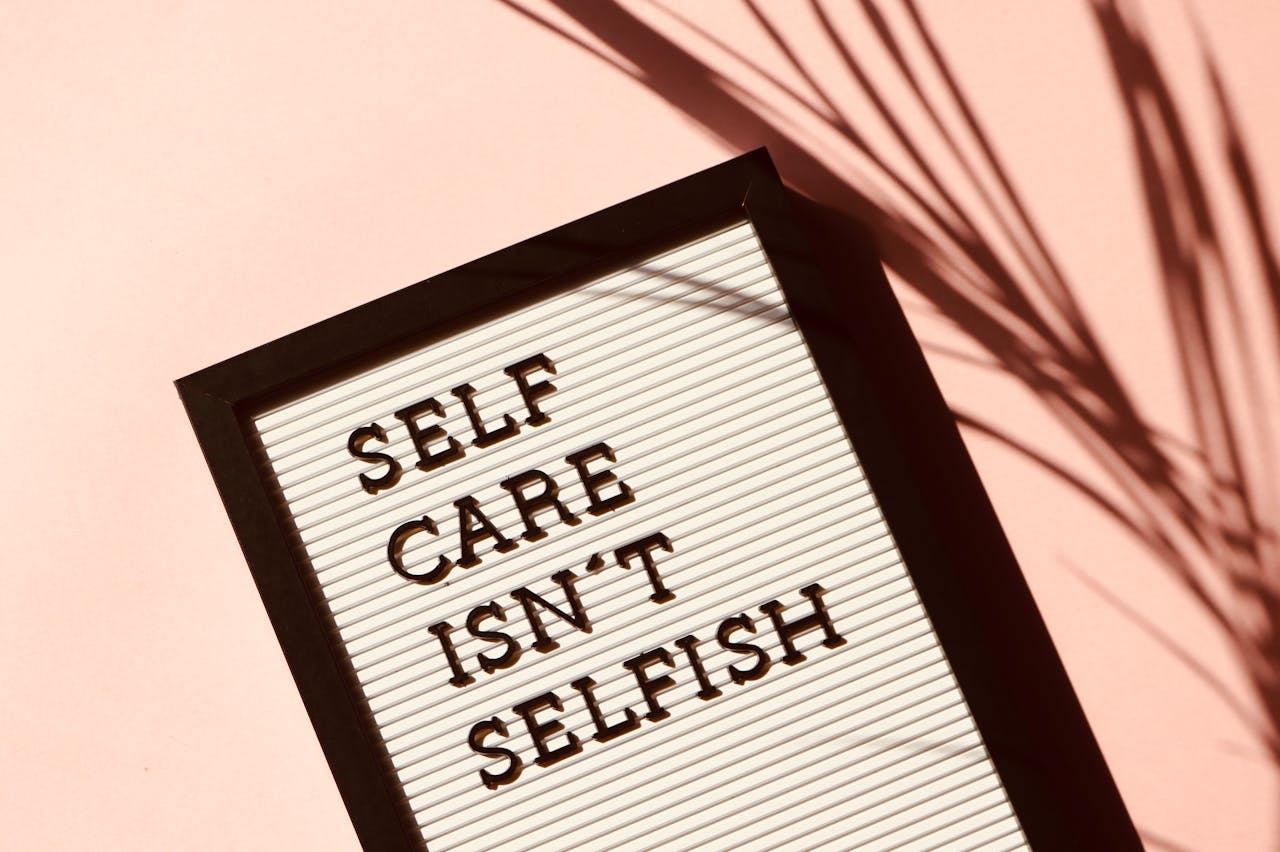 our-services-1 Letter board displaying 'Self Care Isn't Selfish' with artistic shadow on pink background.